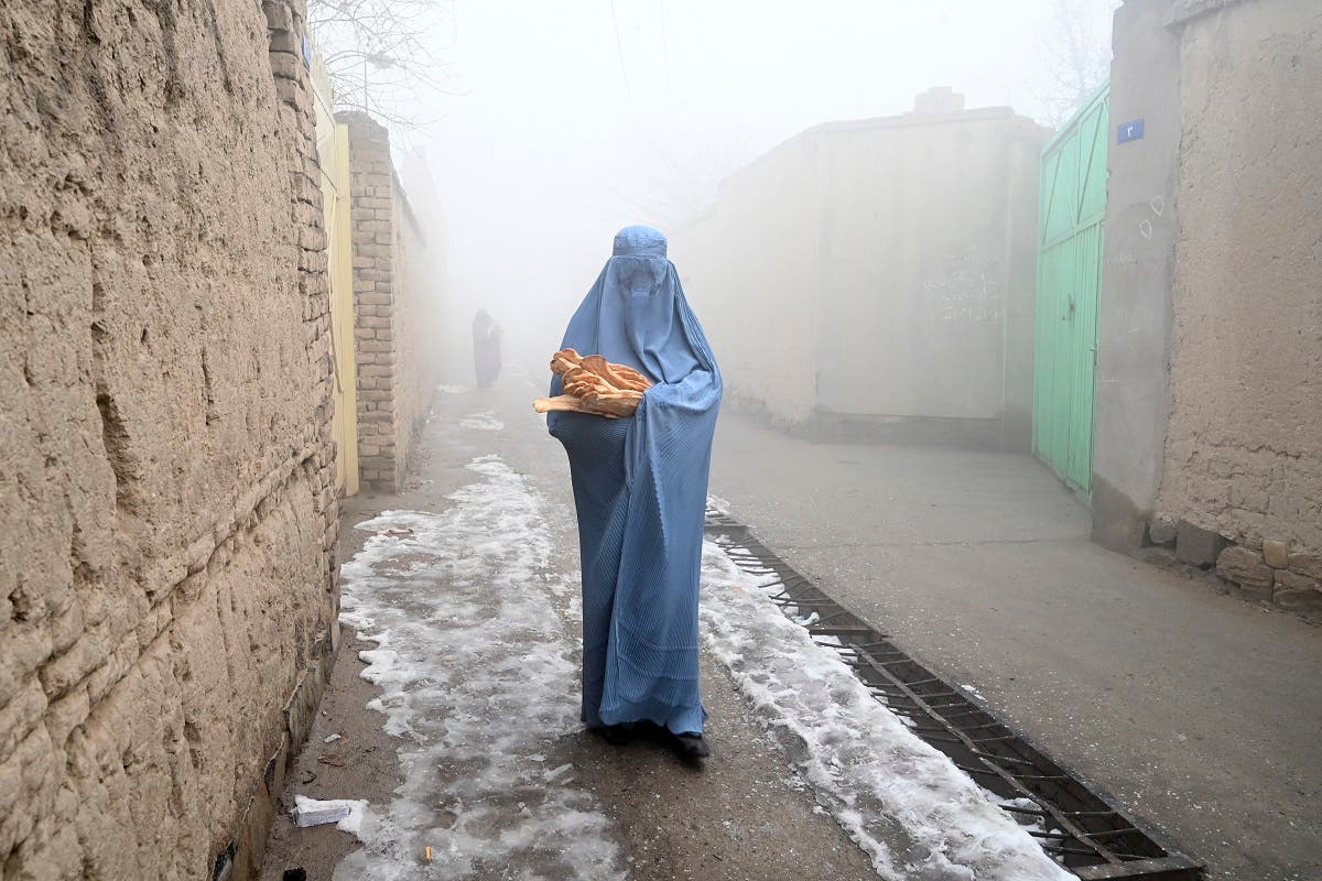 A woman wearing a burqa walks along a road towards her home after receiving free bread distributed as part of the Save Afghans From Hunger campaign in Kabul on January 18, 2022. (AFP)
