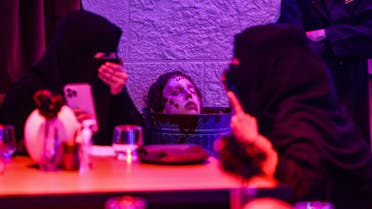 Diners laugh as a zombie head prop is placed near their table at the horror-themed Shadows restaurant in the Saudi capital Riyadh's Boulevard entertainment city, late on January 19, 2022. The restaurant is offering patrons in the conservative kingdom a unique experience, dishes with a side of skull and blood in the company of zombies and vampires. (AFP)