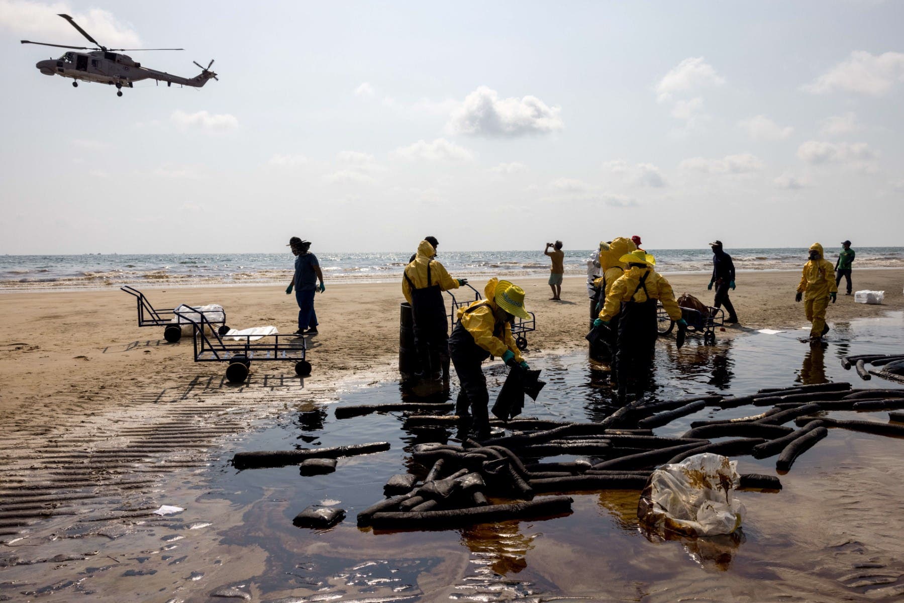 A helicopter flies overhead as workers clean up crude oil on Mae Ram Phueng beach following a spill caused by a leak in an undersea pipeline owned by Star Petroleum Refining Public Company Limited (SPRC) in Rayong on January 29, 2022. (Reuters)