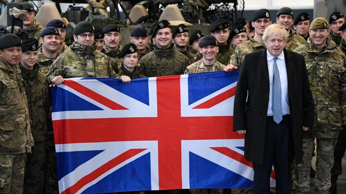 Britain's Prime Minister Boris Johnson (2nd R) poses or a photograph with British troops in front of a Union flag during a visit to Warszawska Brygada Pancerna military base near Warsaw, Poland on February 10, 2022. (AFP)