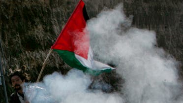 A Palestinian demonstrator holding a Palestinian flag runs away from Israeli soldiers' tear gas during a protest against the construction of the controversial Israeli barrier near the West Bank village of al-Khader, south of Bethlehem, February 22, 2008. REUTERS/Nayef Hashlamoun (WEST BANK)