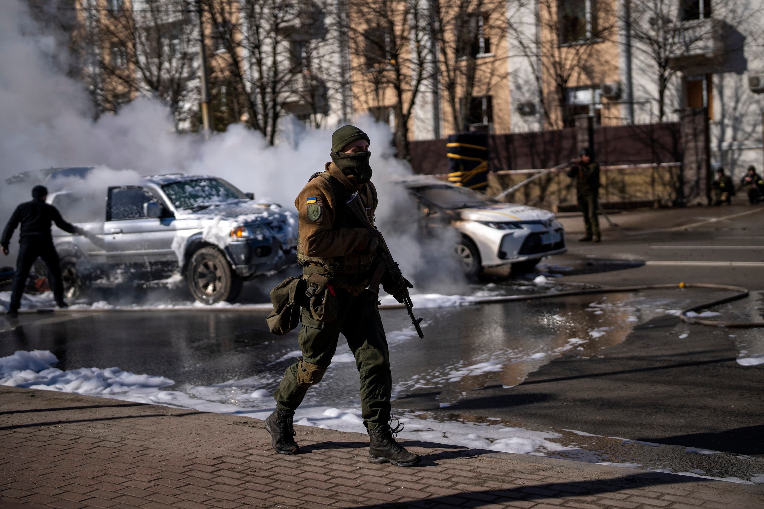 Ukrainian soldiers take positions outside a military facility as two cars burn, in a street in Kyiv, Ukraine, Saturday, Feb. 26, 2022. (AP)