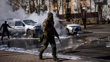 Ukrainian soldiers take positions outside a military facility as two cars burn, in a street in Kyiv, Ukraine, Saturday, Feb. 26, 2022. Russian troops stormed toward Ukraine's capital Saturday, and street fighting broke out as city officials urged residents to take shelter. (AP Photo/Emilio Morenatti)