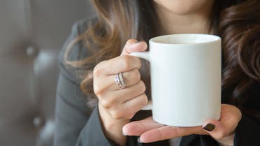Young woman holding a white coffee cup with two hands outdoors. stock photo