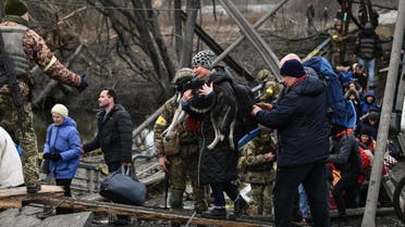 A woman carries a dog while people cross a destroyed bridge as they evacuate the city of Irpin, northwest of Kyiv, during heavy shelling and bombing on March 5, 2022, 10 days after Russia launched a military invasion on Ukraine. (AFP)