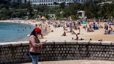 A woman (L) uses her smart phone while people (C) use the beach in Hong Kong on April 13, 2020. (AFP)