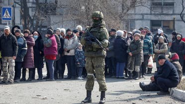 A Russian army soldier stands next to local residents who queue for humanitarian aid delivered during Ukraine-Russia conflict, in the besieged southern port of Mariupol, Ukraine March 23, 2022. (Reuters)