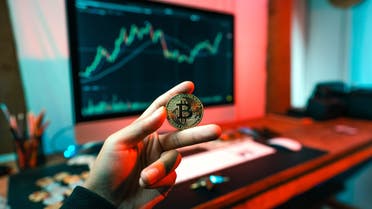 A stock image of cryptocurrency trading, showing a man holding a coin with the Bitcoin logo on it. (Unsplash, Art Rachen)