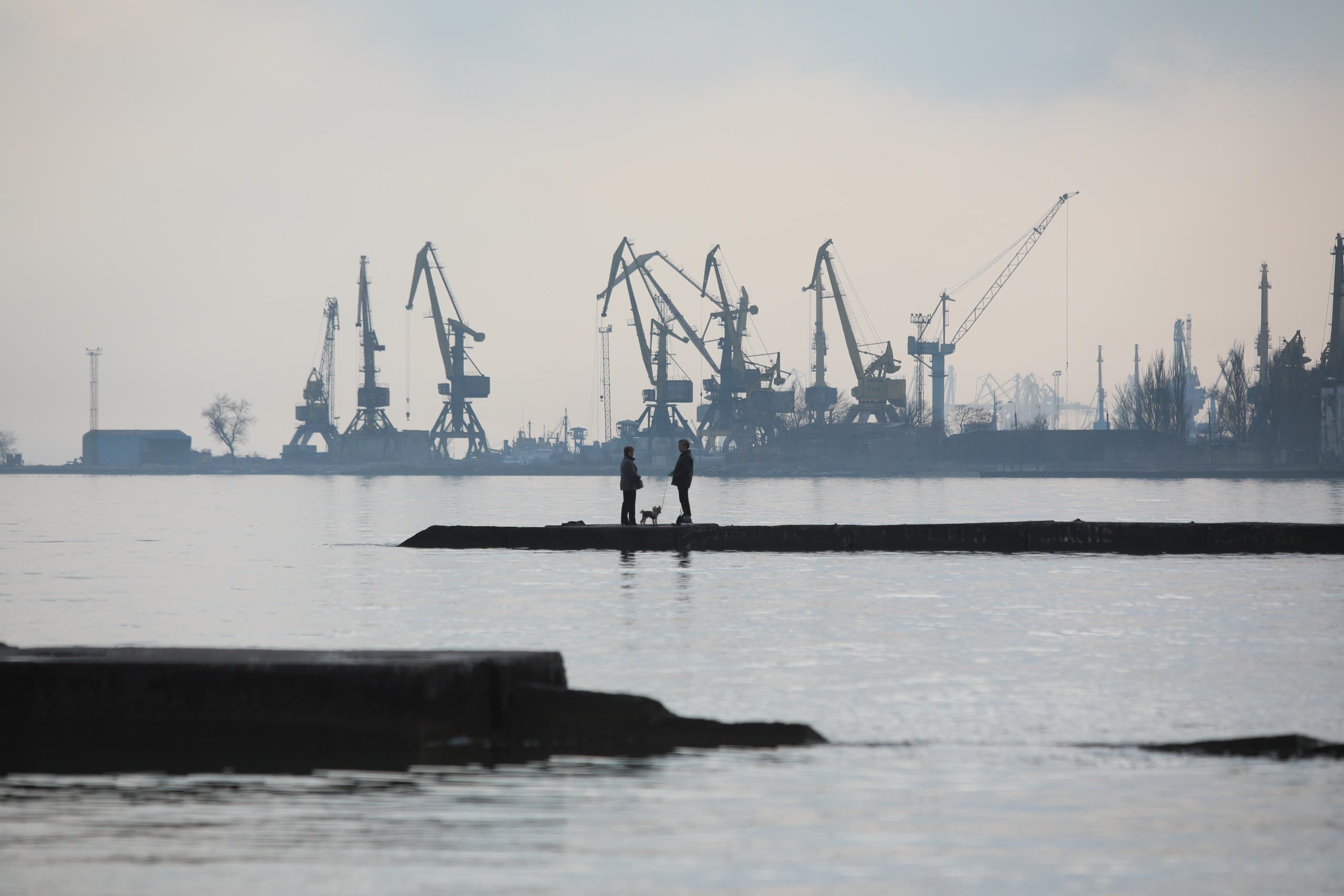 A couple walks a dog on a pier at a coast of the Sea of Azov in Ukraine's industrial port city of Mariupol on February 23, 2022. (AFP)