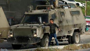 A Palestinian man hurls stones from behind an Israeli security armoured vehicle during a raid to look for wanted Palestinians in Nablus city, in the occupied West Bank. (AFP)
