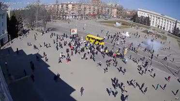 CCTV footage appears to show Russian troops (top, near building) firing stun grenades into a crowd of protesters, some with Ukrainian flags, amid the Russian invasion, along Ushakova Avenue in Kherson, Ukraine, on March 21, 2022 in this still image from video. (Reuters)