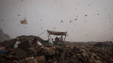 Waste collectors take shelter from heat under a tarpaulin on a hot summer day, as debris and smoke billow following a fire at the Bhalswa landfill site in New Delhi, India, April 29, 2022. (Reuters)