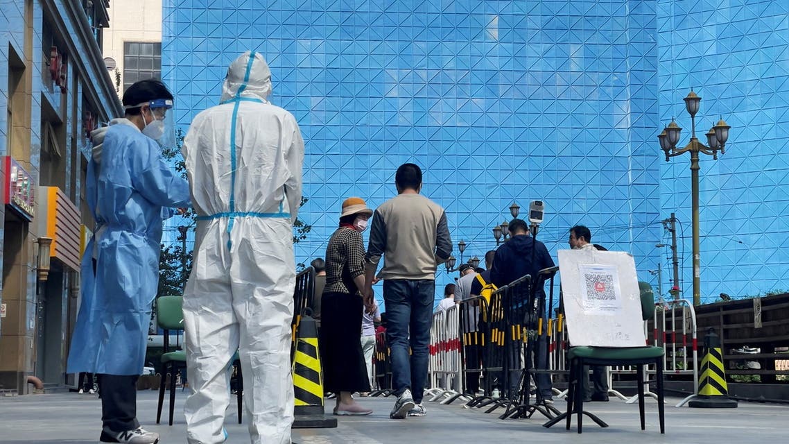 Workers in protective suits stand next to people lining up a makeshift nucleic acid testing site during a mass testing for the coronavirus disease (COVID-19) in Chaoyang district of Beijing, China May 4, 2022. (Reuters)
