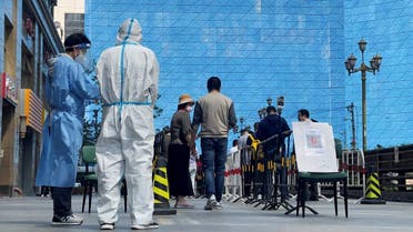 Workers in protective suits stand next to people lining up a makeshift nucleic acid testing site during a mass testing for coronavirus in Chaoyang district of Beijing, China, on May 4, 2022. (Reuters)