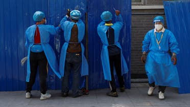 عمال يرتدون معدات الحماية الشخصية يركبون حاجزًا حول منطقة سكنية مغلقة بسبب كورونا- بكين (رويترز)