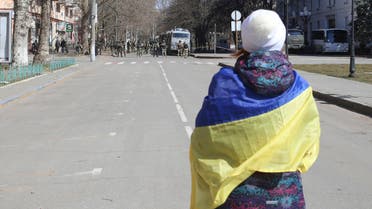 A woman covered by Ukrainian flag stands in front of Russian troops in a street during a rally against Russian occupation in Kherson, Ukraine, Saturday, March 19, 2022. (AP Photo/Olexandr Chornyi)