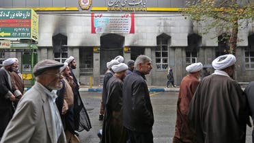A file photo shows Iranians walk past the branch of a local bank that was damaged during demonstrations against petrol price hikes. (File Photo: AFP)