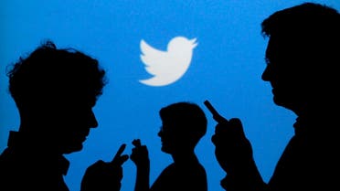 People holding mobile phones are silhouetted against a backdrop projected with the Twitter logo in this illustration picture. (Reuters)