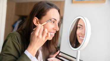Beautiful woman putting make-up on at home using a lighted mirror stock photo
