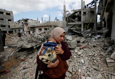 A Palestinian woman carries her child amid the rubble of their houses which were destroyed by Israeli air strikes during the Israel-Hamas fighting in Gaza May 23, 2021. (File photo: Reuters)