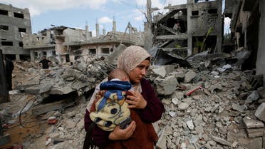 A Palestinian woman carries her child amid the rubble of their houses which were destroyed by Israeli air strikes during the Israel-Hamas fighting in Gaza May 23, 2021. REUTERS/Mohammed Salem