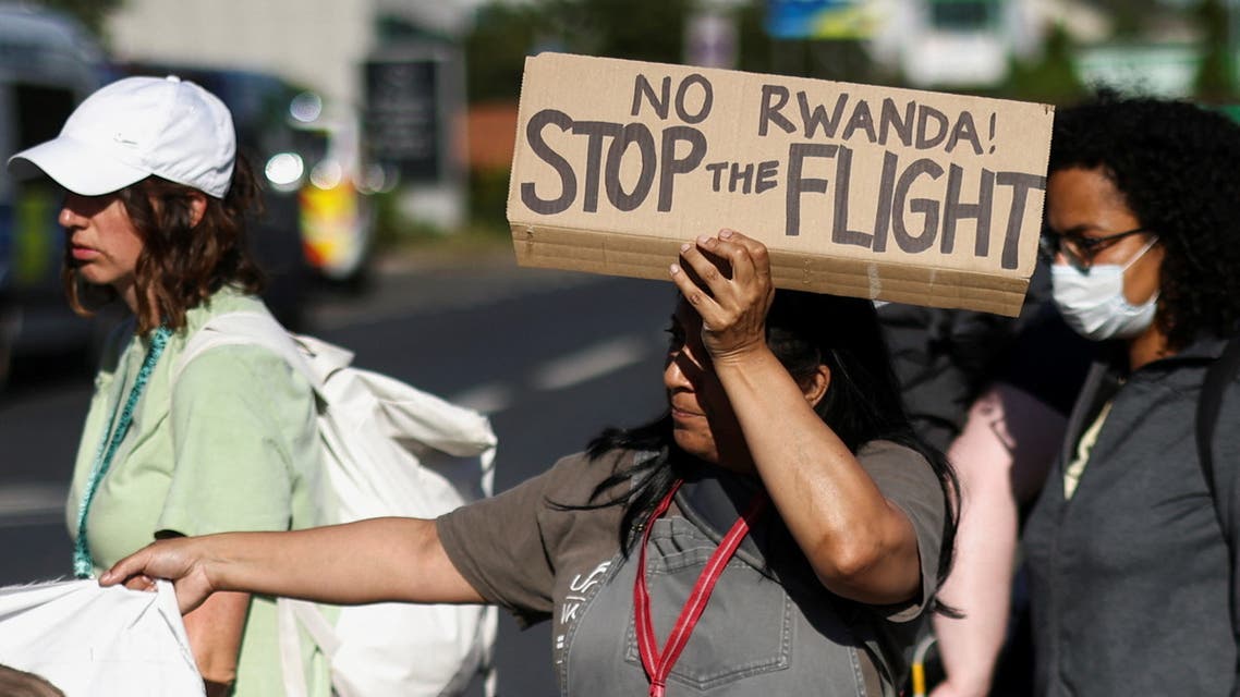 An activist blocking a road leading away from the Colnbrook Immigration Removal Centre holds a banner during a protest against the British Governments plans to deport asylum seekers to Rwanda, near Heathrow airport in London, June 14, 2022. (Reuters)