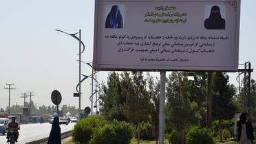 A burqa-clad woman walks past a hoarding placed by Taliban authorities asking women to wear a hijab, in Kandahar on June 16, 2022. (AFP)