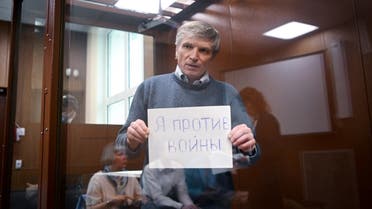 Moscow city deputy Alexei Gorinov, accused of spreading “false information” about the Russian army, holds a sheet of paper reading “I am against war” inside a glass cell during a hearing in his trial at a courthouse in Moscow on June 21, 2022. (AFP)