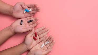 Kid's hands with colorful pharmaceutical medicine capsules on pink background stock photo