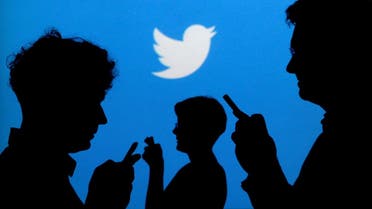 People holding mobile phones are silhouetted against a backdrop projected with the Twitter logo in this illustration. (Reuters)