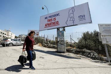 A Palestinian woman walks in front of a billboard ahead of the visit of US President Joe Biden in Bethlehem in the Israeli-occupied West Bank, on July 13, 2022. (Reuters)