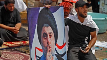 A supporter of Iraqi Shia cleric Muqtada al-Sadr sits with his portrait during the weekly Friday prayers at the vigil outside parliament headquarters in the capital Baghdad's high-security Green Zone on August 26, 2022. (AFP)