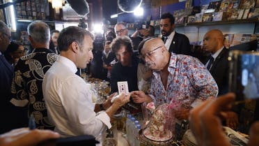 France’s President Emmanuel Macron (L) receives a gift from Boualem Benhaoua (2ndR), owner of the Disco Maghreb Shop in, mythical label of rai music, as France’s former minister and Arab World Institute President Jack Lang (C) looks on during his visit in Oran on August 27, 2022. (AFP)