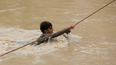A boy crosses a flooded street, with the help of a wire fastened on both ends, following rains and floods during the monsoon season in Charsadda, Pakistan August 27, 2022. (Reuters)