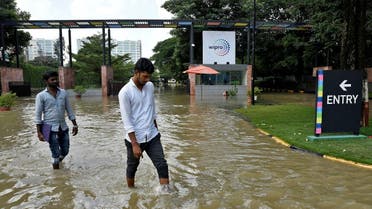 People wade through a waterlogged road in front of the entrance of IT major Wipro Ltd following torrential rains in Bengaluru, India, on September 5, 2022. (Reuters)