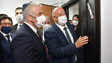 The head of the Israeli diplomatic delegation David Govrin (R), hanging a mezuzah (doorpost) on the door of the new Israeli liason office, as alternate prime minister and Foreign Minister Yair Lapid (L) looks on, during an inaugural ceremony in the capital Rabat, 11, 2021. (Israeli Ministry of Foreign Affairs/AFP) 