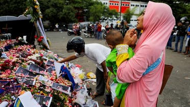 A woman carrying her child prays on a monument as she pays condolence to the victims after a riot and stampede following soccer match between Arema vs Persebaya, outside the Kanjuruhan stadium in Malang, East Java province, Indonesia, on October 3, 2022. (Reuters)