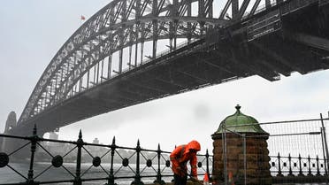 A construction worker sweeps away water while it rains next to the Harbour Bridge in Sydney on October 6, 2022. (Photo by Muhammad FAROOQ / AFP)