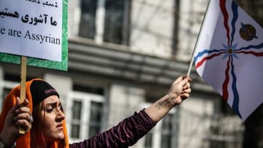 فتاة تحمل بيد العلم الأشوري وبيد الأخرى لافتة كتب عليها نحن آشوريون