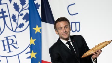French President Emmanuel Macron holds a baguette during a reception honoring the French community in the US, at the French Embassy in Washington, DC, on November 30, 2022. (AFP)
