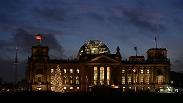 A German flag flutters on the Reichstag building that houses the Bundestag (lower house of parliament) in Berlin is illuminated on early December 8, 2021. (AFP)