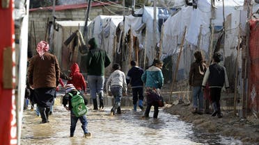 Refugees walk through flood water and mud covering the ground at an informal tent settlement housing Syrian refugees following winter storms in the area of Delhamiyeh, in the central Bekaa Valley on January 17, 2019. (AFP)