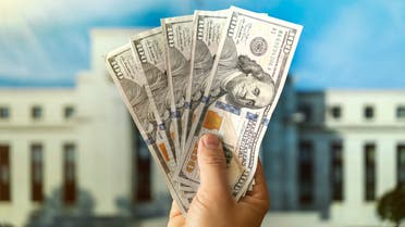 دولارات في يد رجل وفي الخلفية مبنى الاحتياطي الفيدرالي في واشنطن iStock