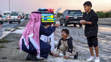 A man and children toss handfuls of hail particles picked up off the side of a road after a storm in the Umm al-Haiman district, about 55 kilometres south of Kuwait City, on December 27, 2022. (AFP)
