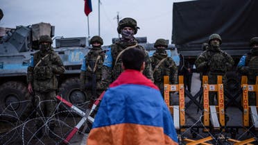 A protester wearing the Armenian national flag stands in front of Russian peacekeepers blocking the road outside Stepanakert, capital of the self-proclaimed Nagorno-Karabakh region of Azerbaijan, on December 24, 2022. Russia's Foreign Minister Sergei Lavrov on December 23, 2022 called for de-escalation in Azerbaijan's Armenian-populated Nagorno-Karabakh, a region which has sparked two wars between the Caucasus neighbours. (Photo by Davit GHAHRAMANYAN / AFP)