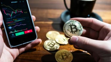 Stock image of a man holding a physical bitcoin while using his smartphone to invest in cryptocurrency. (Unsplash, Wance Paleri)