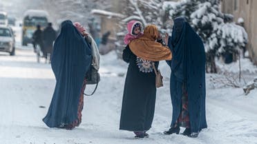 Afghan burqa-clad women carry children as they walk along a snow laden street in Kabul on January 23, 2023. (AFP)