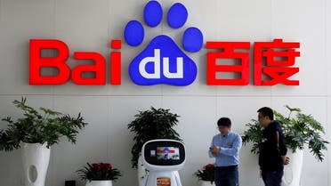 Men interact with a Baidu AI robot near the company logo at its headquarters in Beijing. (Reuters)