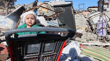 A child sits in a shopping cart at the site of a collapsed building, in the aftermath of a deadly earthquake in Hatay, Turkey, February 8, 2023. (Reuters)