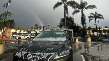 A rainbow appears between palm trees as hail partially covers a vehicle during a winter storm that blanketed the region with rain, snow, and hail in Redondo Beach, California, on February 25, 2023. (AFP)